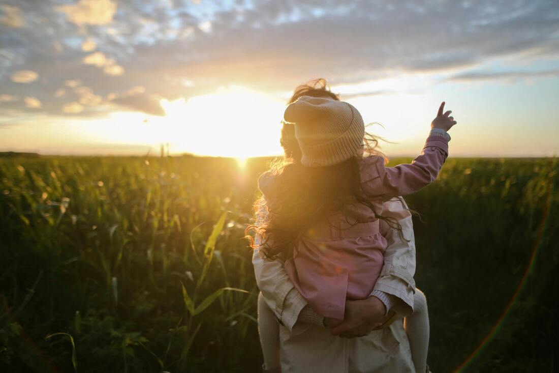 Photo of parent and child in a field with a sunset behind them.
